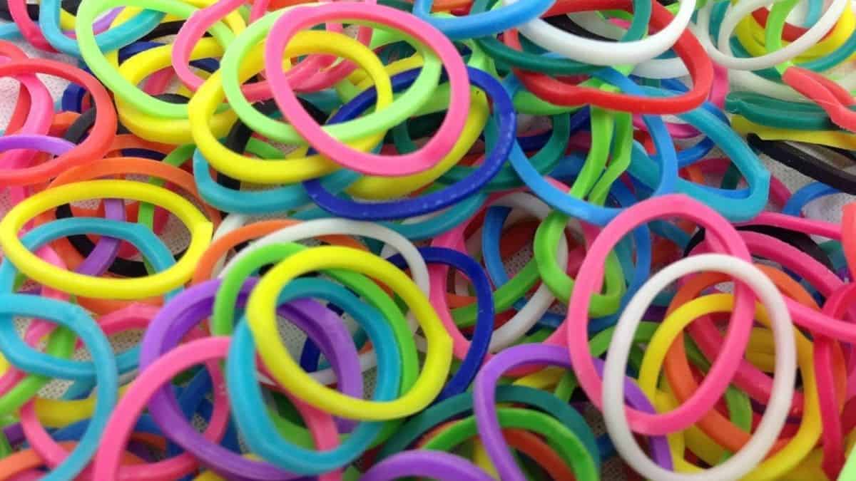 A close-up of colorful loom bands scattered in a pile, showing bright shades of pink, yellow, blue, green, purple, black, and white.