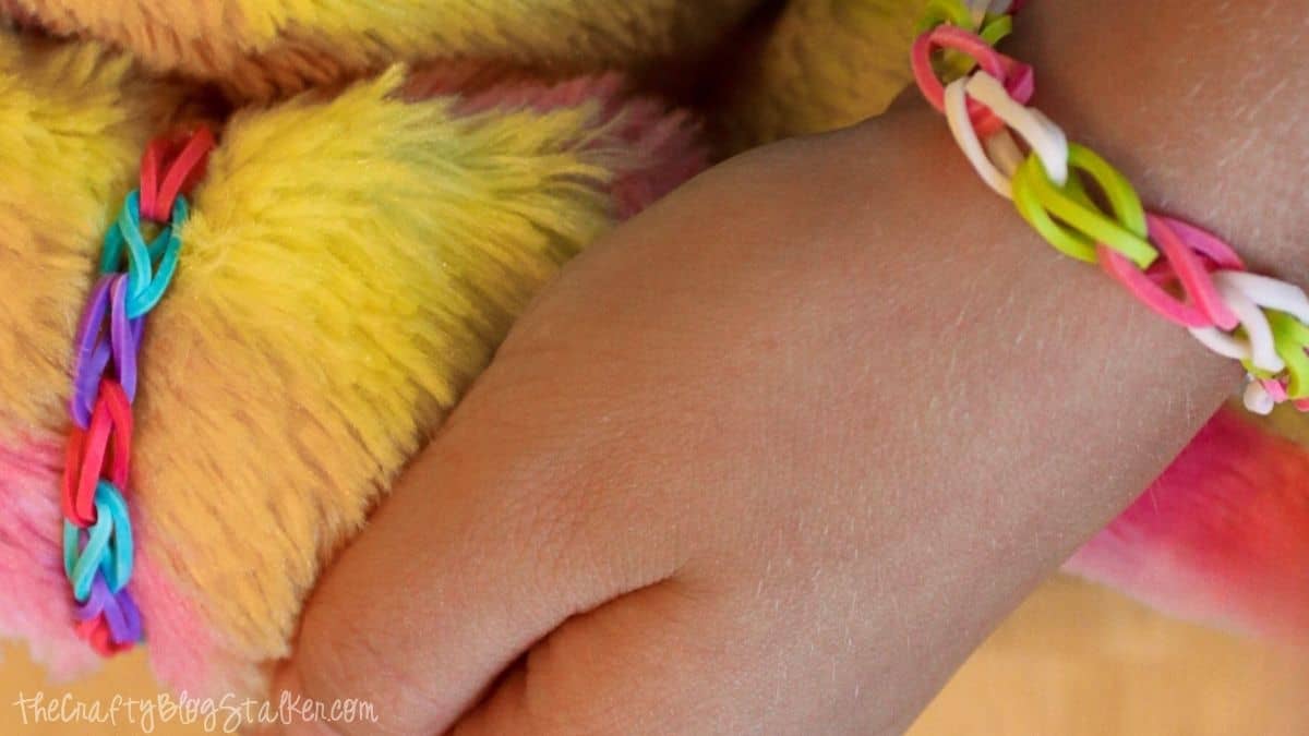 Child wearing a loom band bracelet, and a matching bracelet on her bear's wrist.