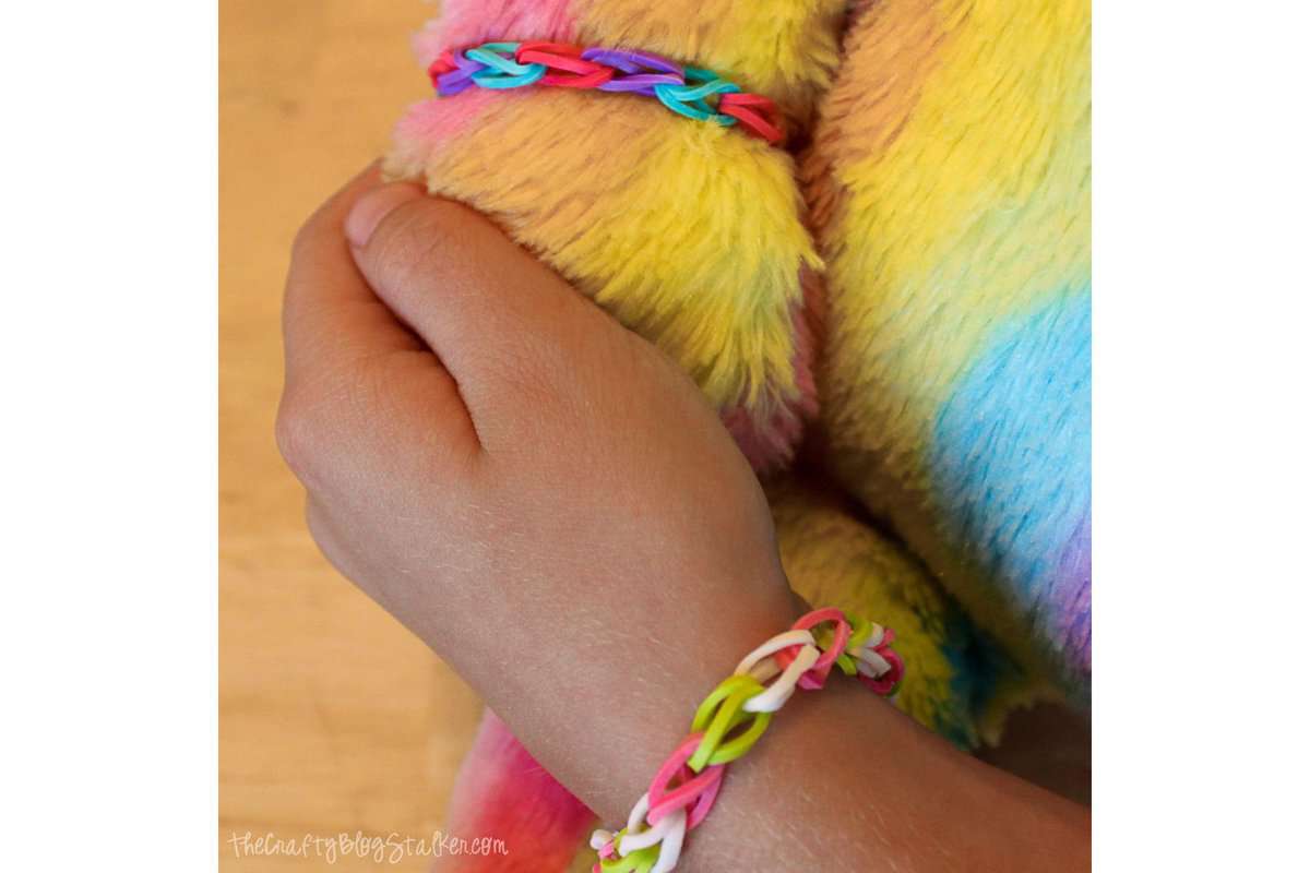 A girl's hand holding a teddy bear's paw, wearing matching rubber band bracelets.