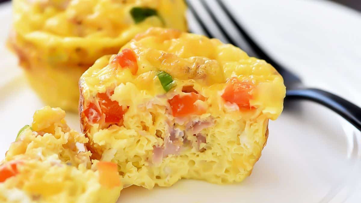 Mini scrambled egg muffins filled with diced ham, peppers, and cheese, served on a white plate.
