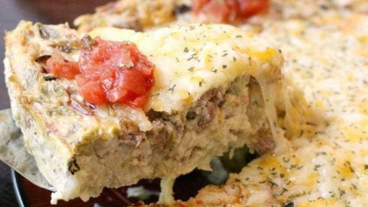 A slice of cheesy Southwest breakfast casserole lifted from the dish, filled with sausage, veggies, and topped with salsa.