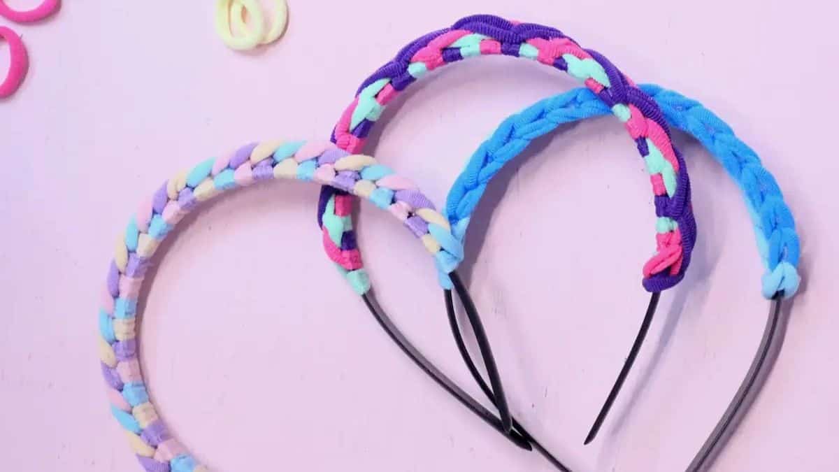 Three colorful braided hair tie headbands in pastel and neon shades displayed on a light pink background.