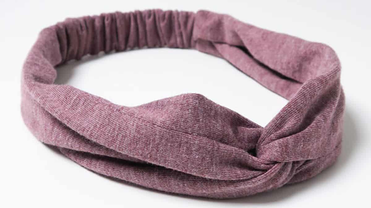 Dusty pink twisted turban stretch headband with gathered elastic back displayed on a light gray background.