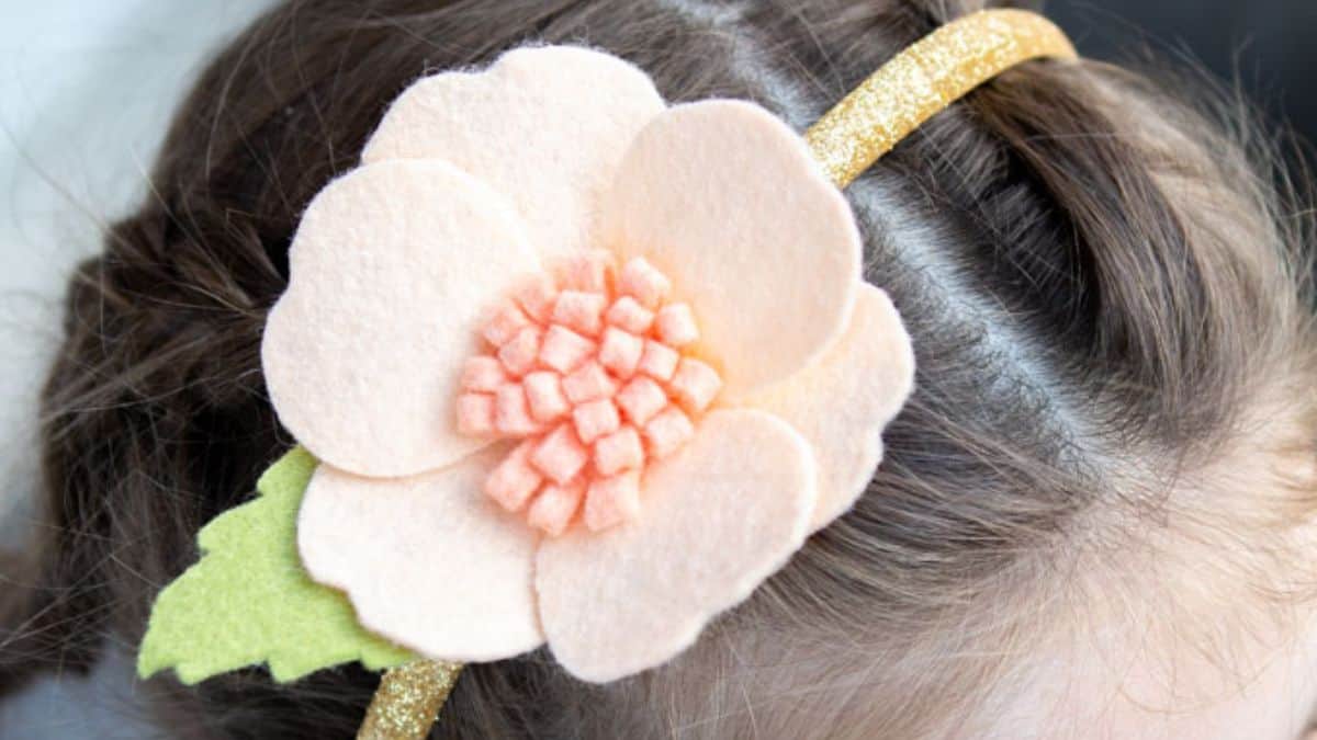 Close-up of a girl wearing a gold glitter headband with a large blush pink felt flower and green felt leaf detail.