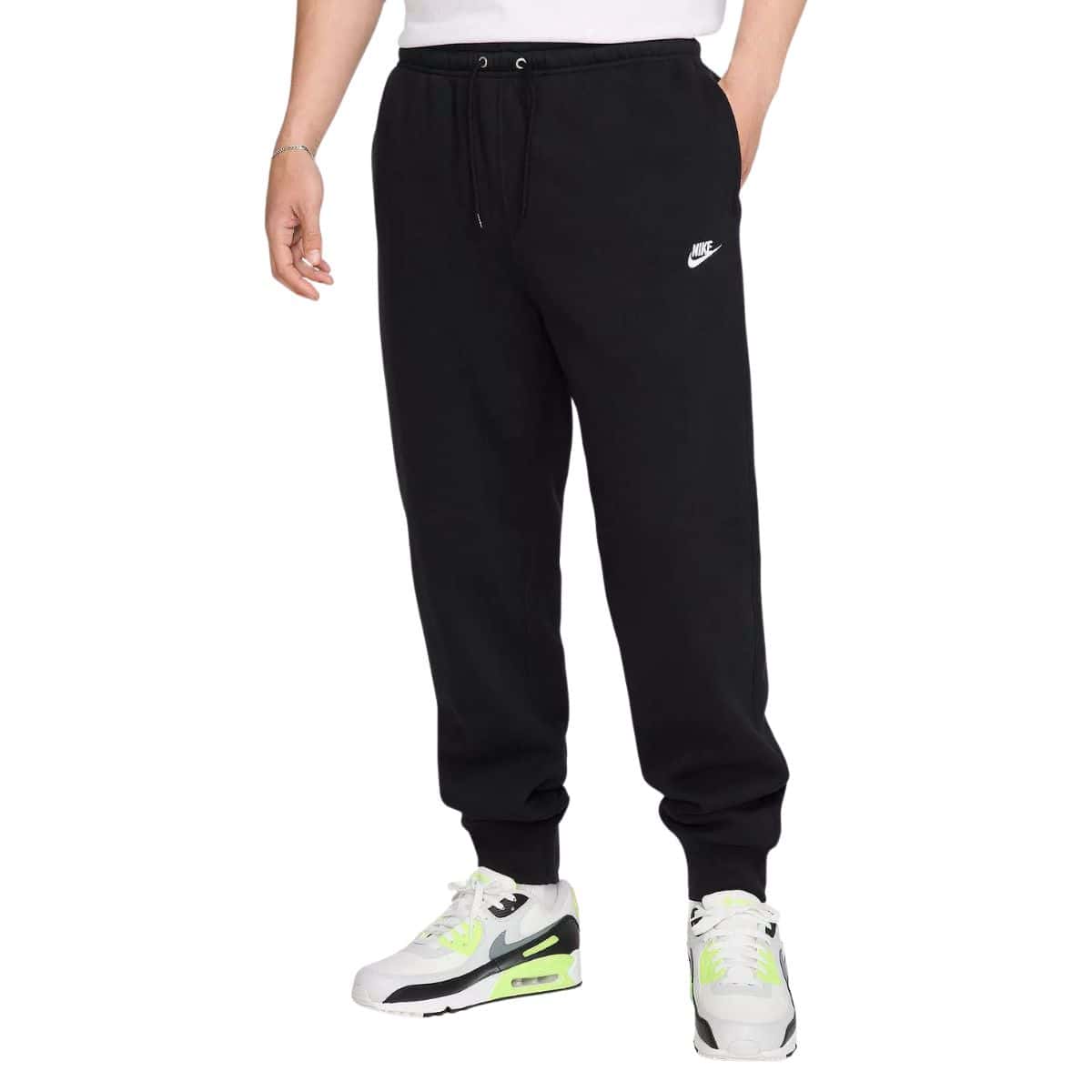 Man wearing black Nike jogger sweatpants with drawstring waist and white logo, paired with white and neon green Nike sneakers.