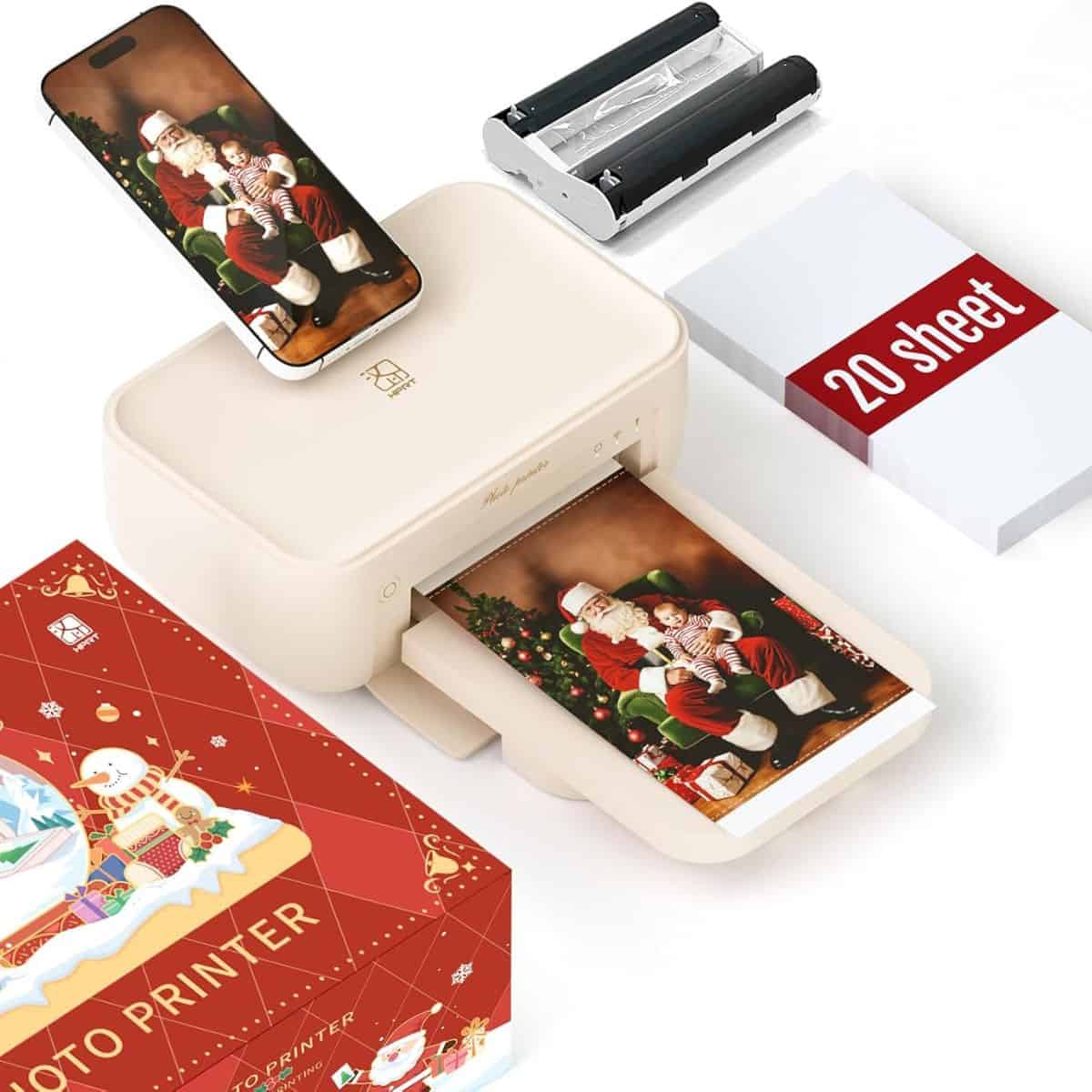 Compact beige photo printer printing a Christmas photo of Santa with a child, shown with smartphone, ink cartridge, and 20-sheet photo paper pack.