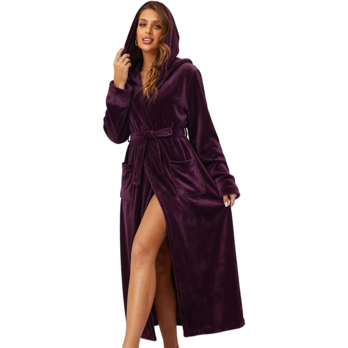 Woman wearing a long beige hooded bathrobe with a belt and front pockets, standing barefoot and smiling.