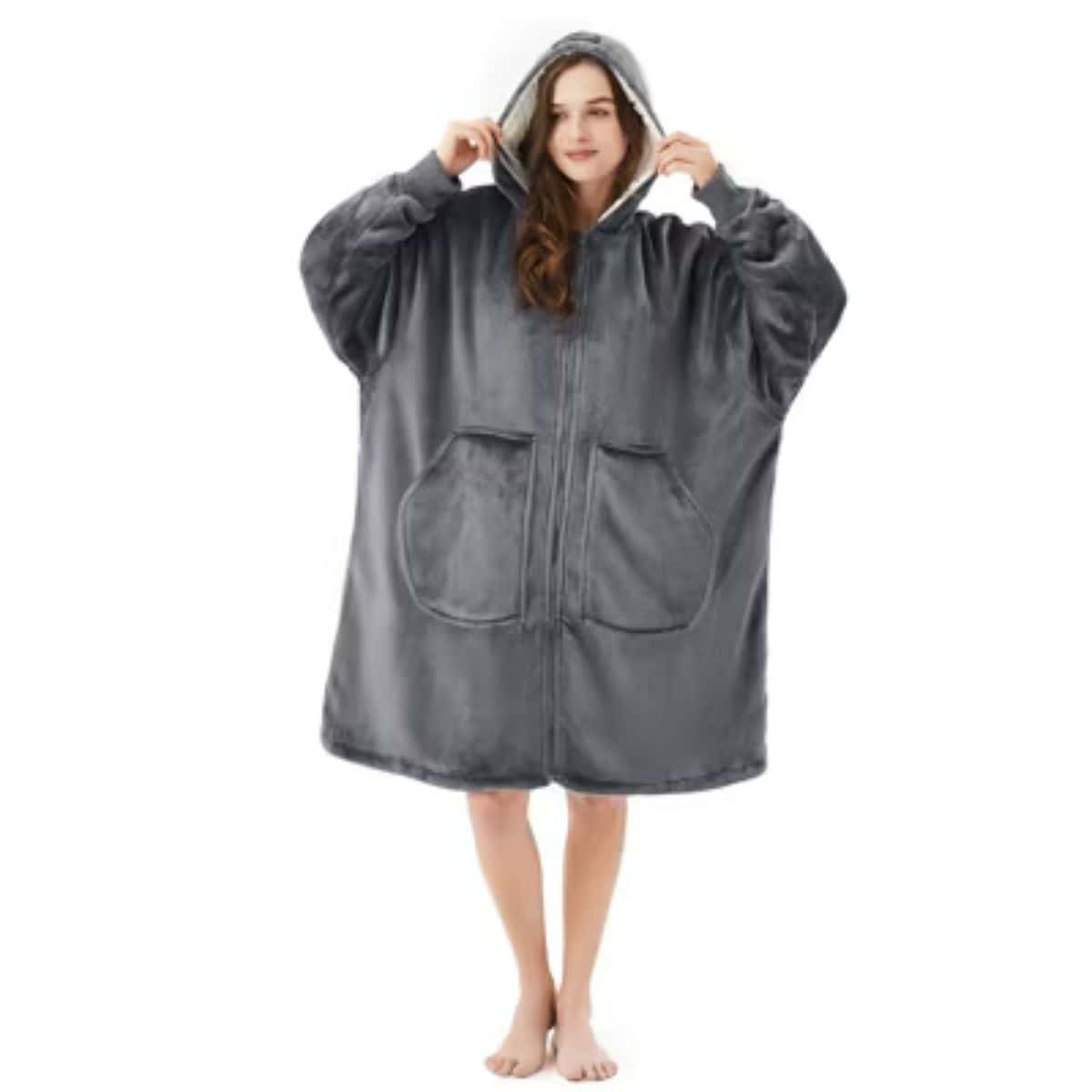 Woman wearing an oversized gray hooded wearable blanket with front pockets, standing barefoot against a white background.