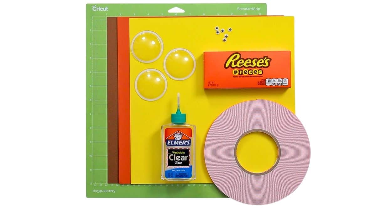 Supplies for candy turkey treats, including colored cardstock, Cricut mat, clear domes, googly eyes, Reese's Pieces, glue, and foam tape.