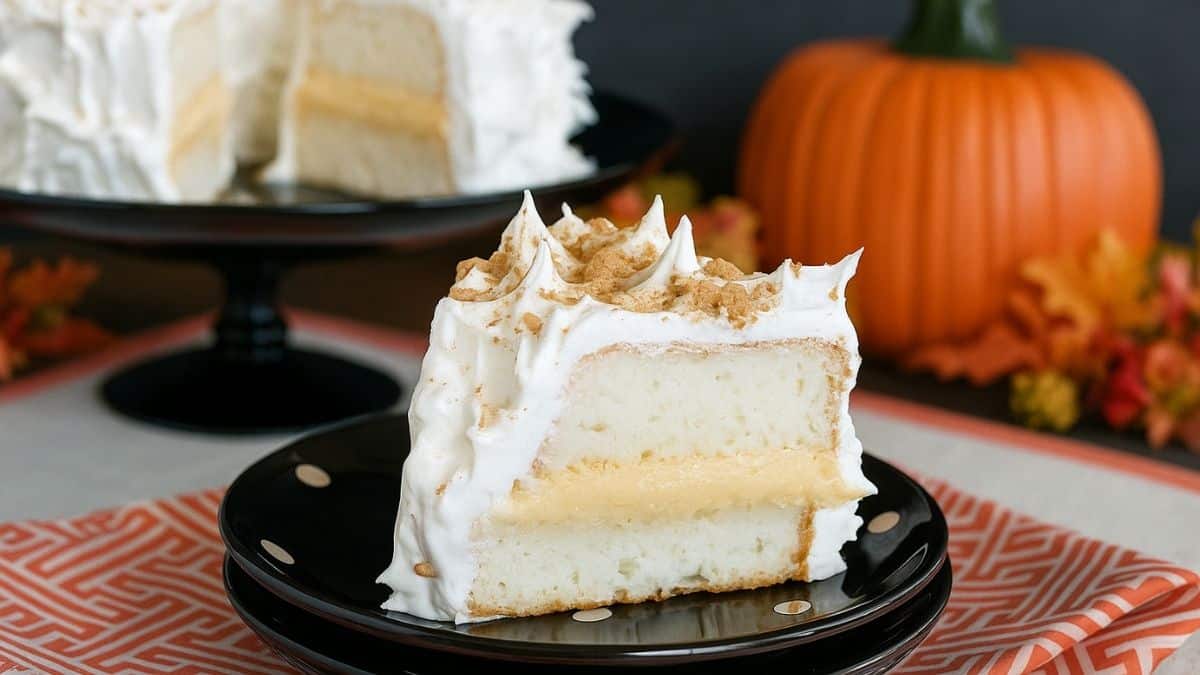Slice of pumpkin toffee angel food cake with fluffy whipped topping and crushed toffee pieces, served on a black plate with a pumpkin in the background.