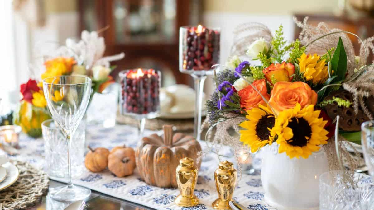 Thanksgiving table with sunflowers, roses, candles filled with cranberries, and small pumpkins creating a bright and festive fall centerpiece.