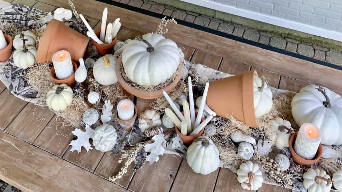 Rustic fall table centerpiece with white pumpkins, terracotta pots, candles, and natural accents arranged on a wooden dining table.