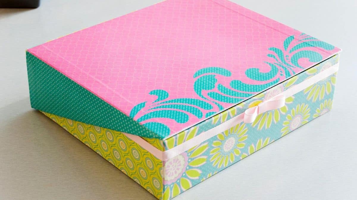 Decorative handmade box covered in patterned paper with a fitted lid and ribbon closure, sitting on a tabletop.
