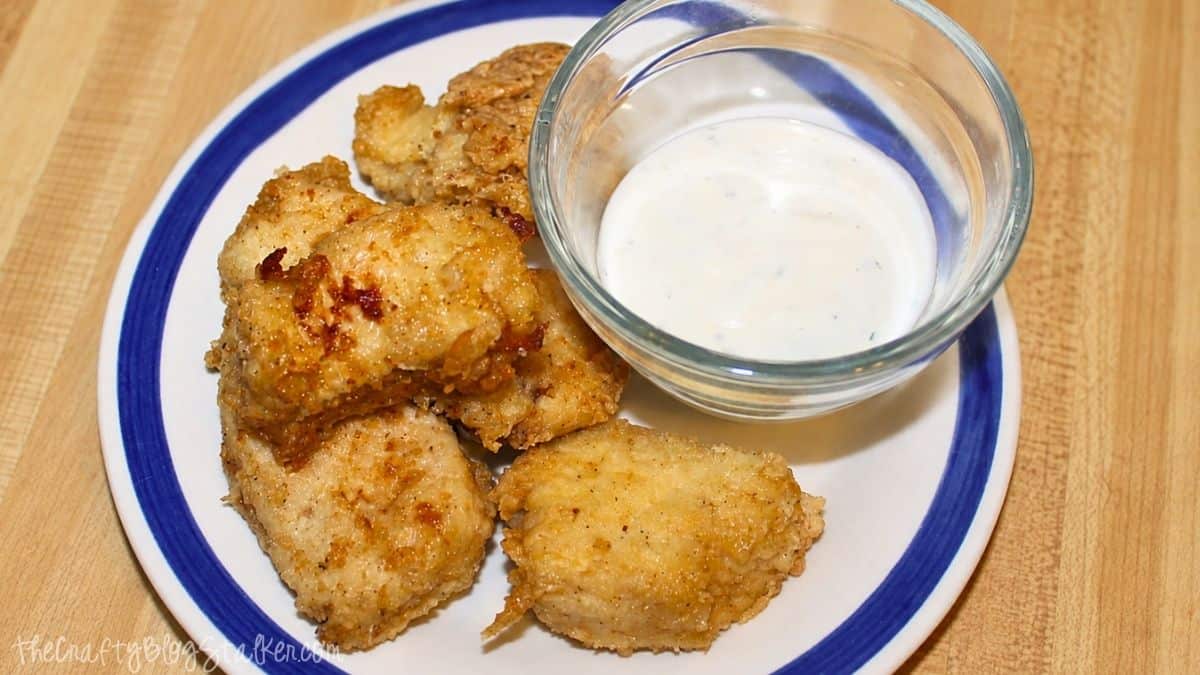 Plate of homemade chicken nuggets served with a small bowl of ranch dipping sauce on a white plate with a blue rim.