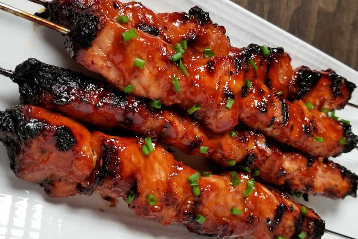 Grilled BBQ pork skewers glazed in a sweet and savory Filipino marinade, topped with chopped green onions and served on a white platter.