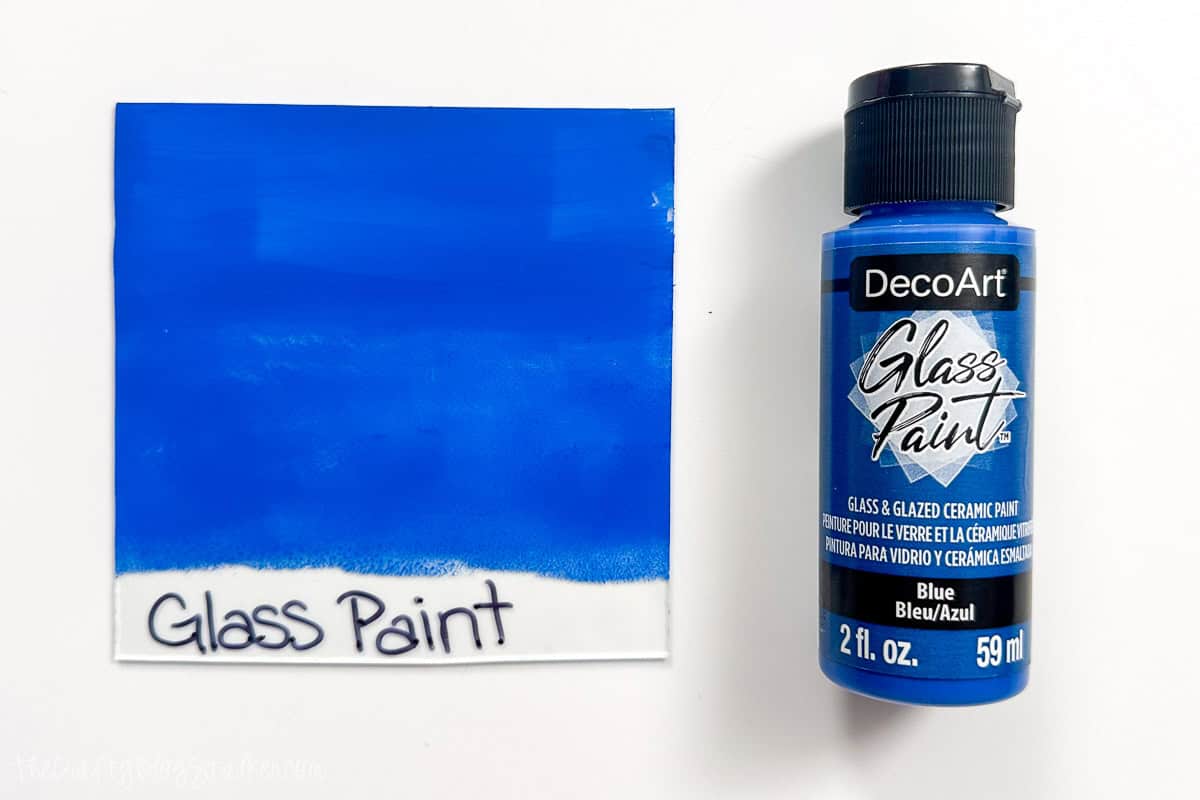 A bottle of Deco Art blue glass paint next to a glass pane painted with the same paint.