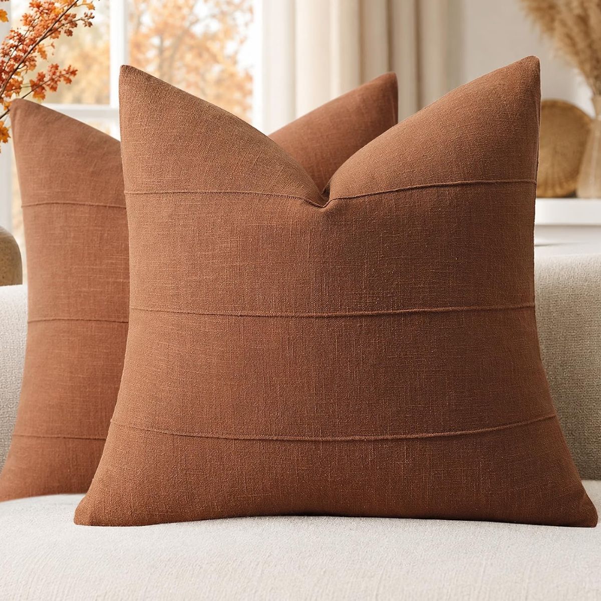 Rust brown linen throw pillows with subtle horizontal seams arranged on a neutral sofa with fall decor in the background.