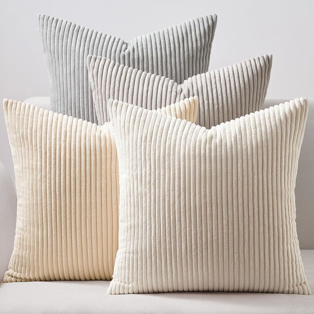 Neutral corduroy throw pillows in soft cream, beige, and light gray arranged on a sofa.