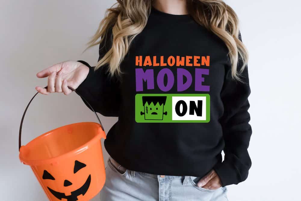 Woman wearing a black sweatshirt with a design that reads 'Halloween Mode: On'.