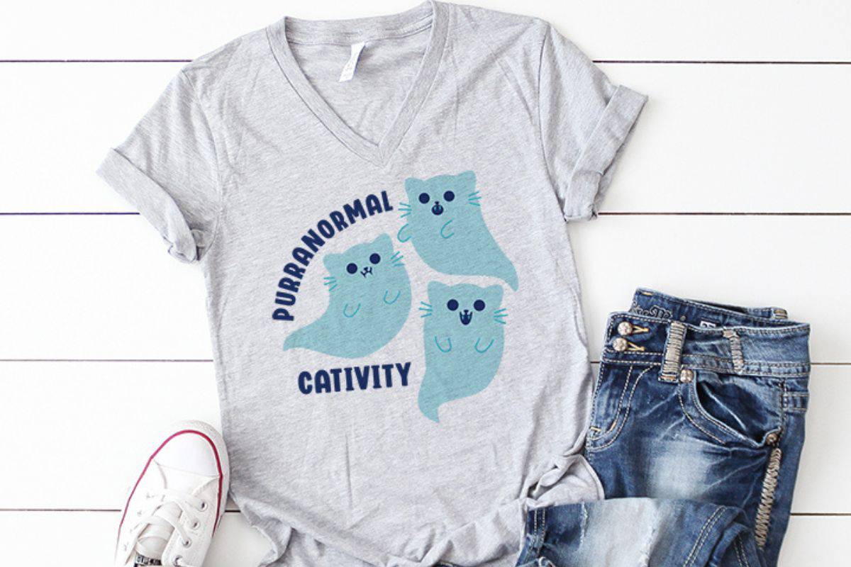 A grey t-shirt with a design with cat ghosts that reads 'Purranormal Cativity'.