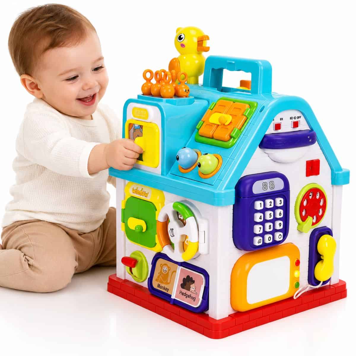 Smiling baby playing with a colorful house-shaped activity cube featuring buttons, switches, a toy phone, and moving parts.
