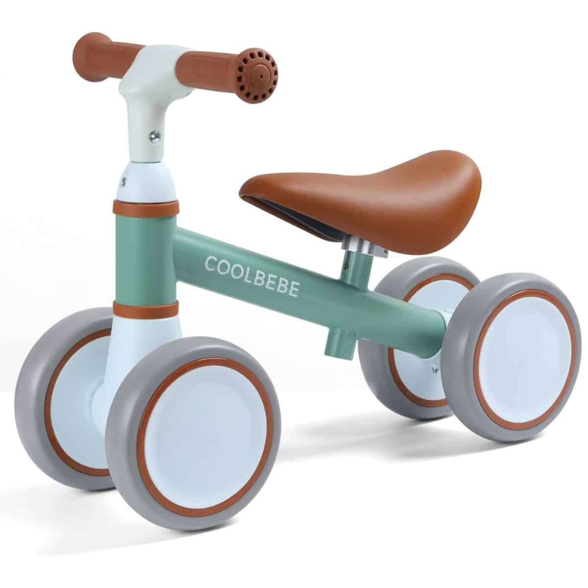 Green and white baby balance bike with four gray wheels, brown seat, and brown handlebars, shown from a side angle.