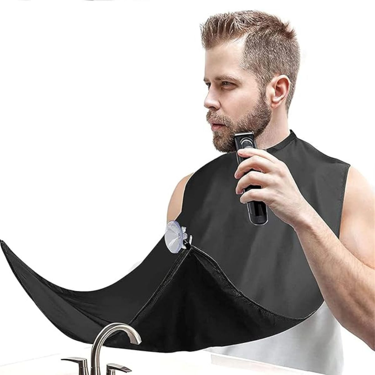 Man trimming his beard while wearing a black beard bib attached to the mirror to catch hair trimmings over the sink.