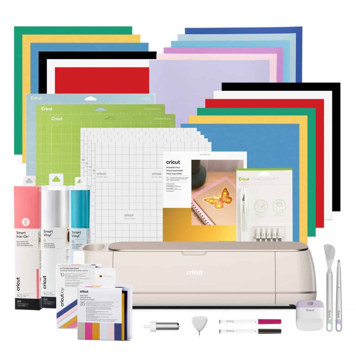 A Cricut Maker machine displayed with cutting mats, vinyl rolls, tools, pens, and stacks of colorful crafting materials included in the bundle.