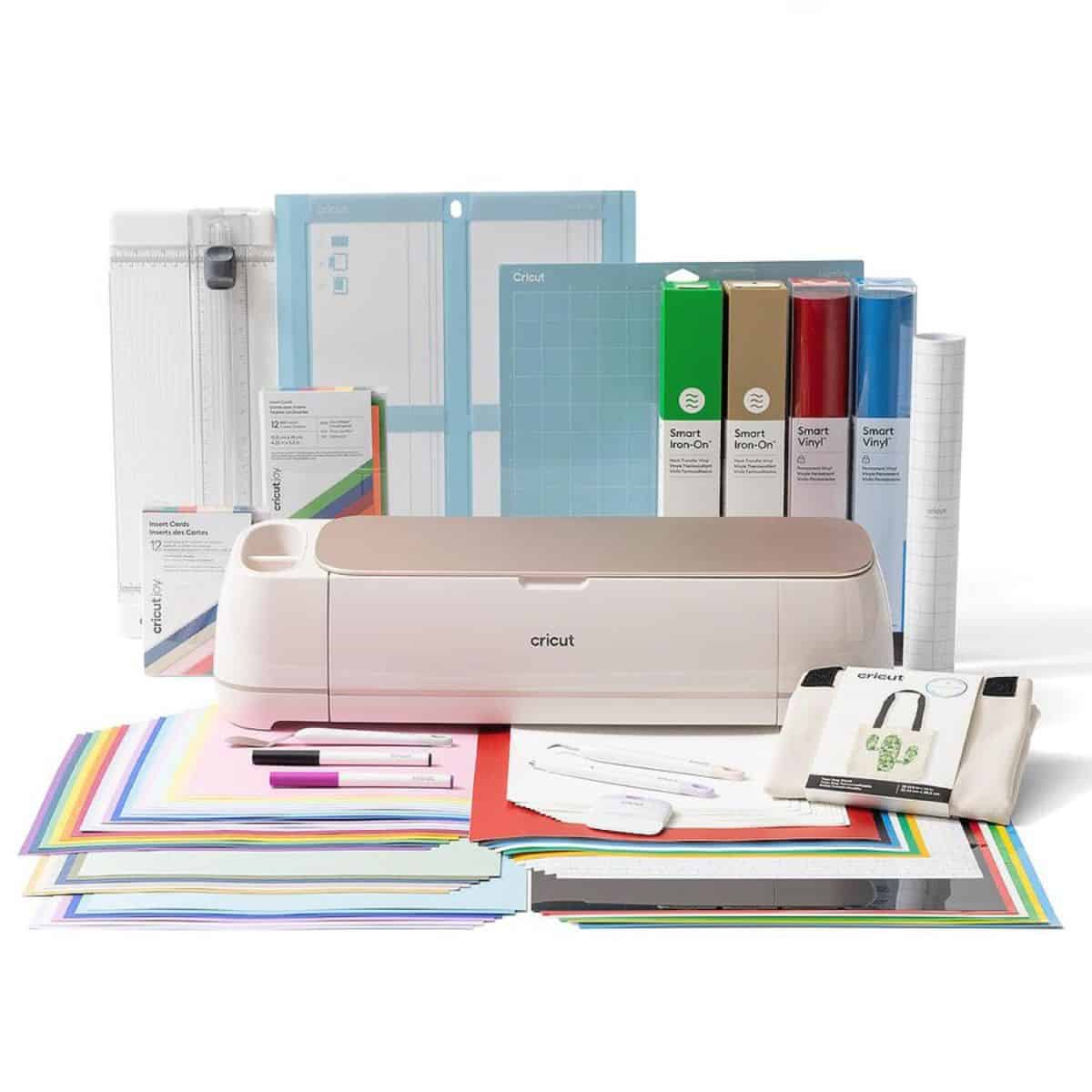 A Cricut Maker machine surrounded by cutting mats, vinyl rolls, tools, sample materials, and colorful crafting sheets from a full Cricut bundle.