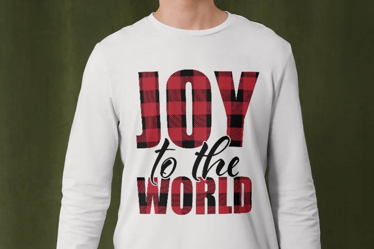 Man wearing a long sleeve t-shirt with a plaid design that reads, Joy To The World.