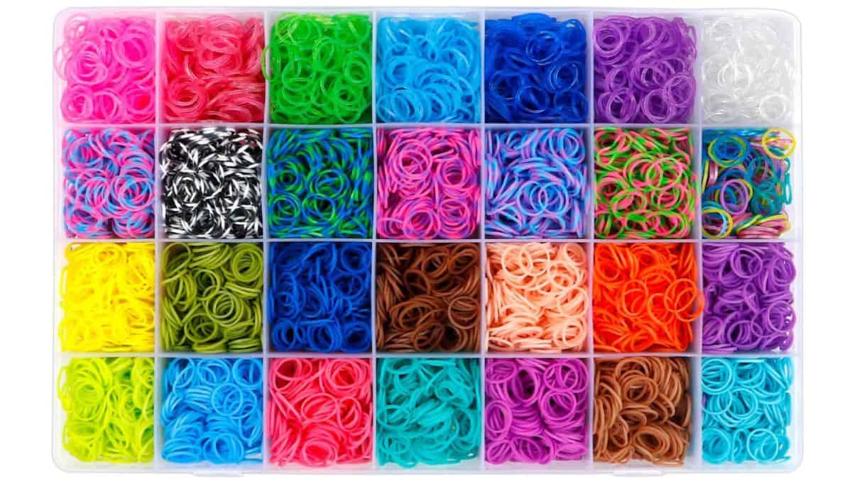 Organizer tray filled with colorful rubber loom bands arranged in separate compartments, showing a variety of bright solid and patterned colors.