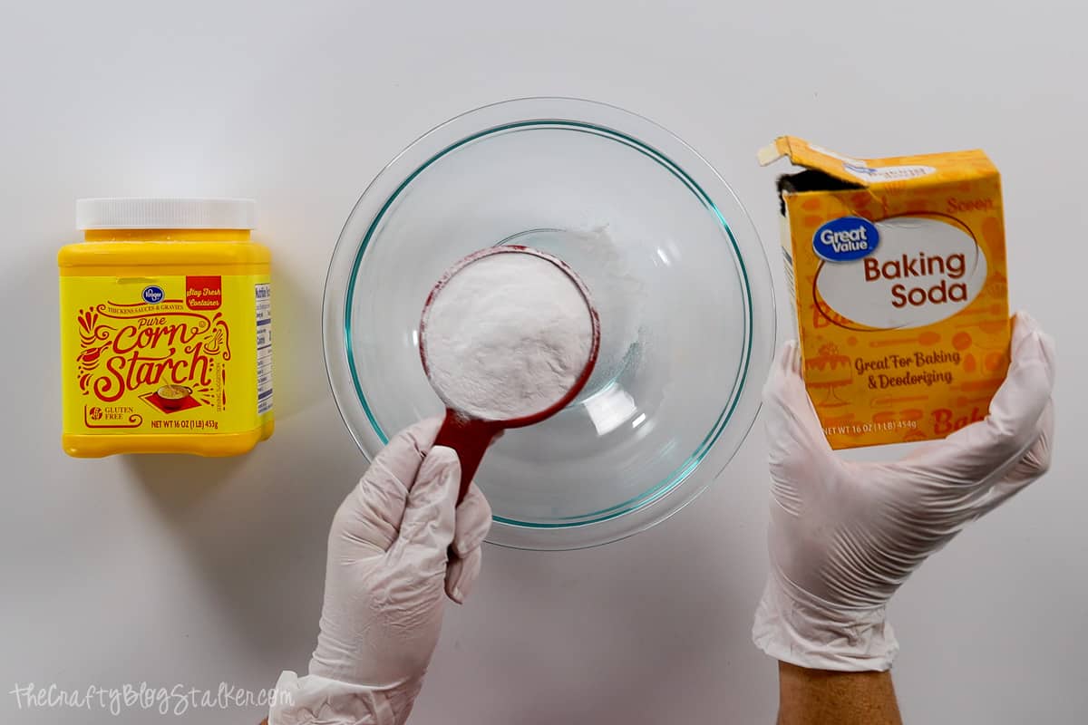 Baking soda and cornstarch being added to a bowl with a measuring cup.