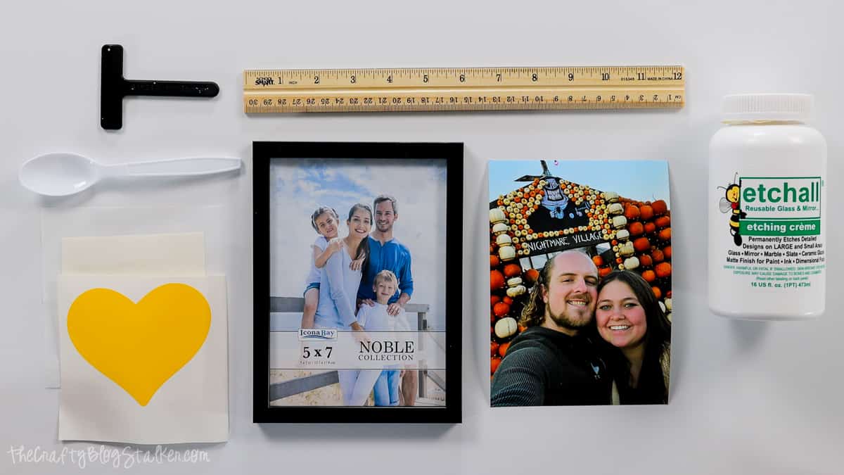 A heart stencil, picture frame, printed photograph, Etchall Etching Creme, ruler, squeegee, and a plastic spoon.
