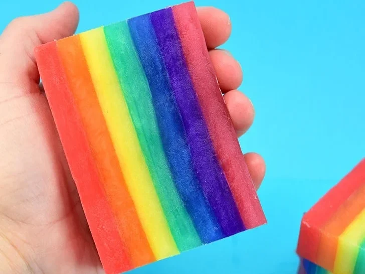 Rainbow layered soap held in one hand.