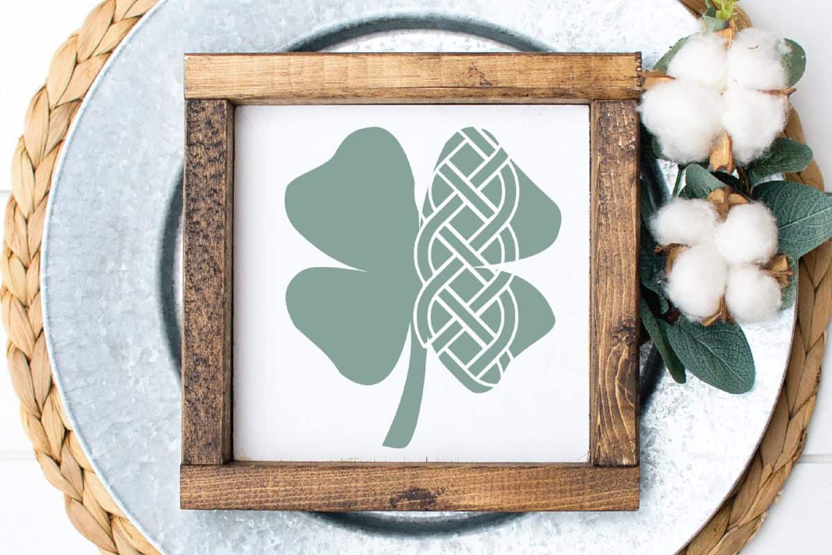 A white sign with a wooden frame that has a design of a celtic knot in a four leaf clover.