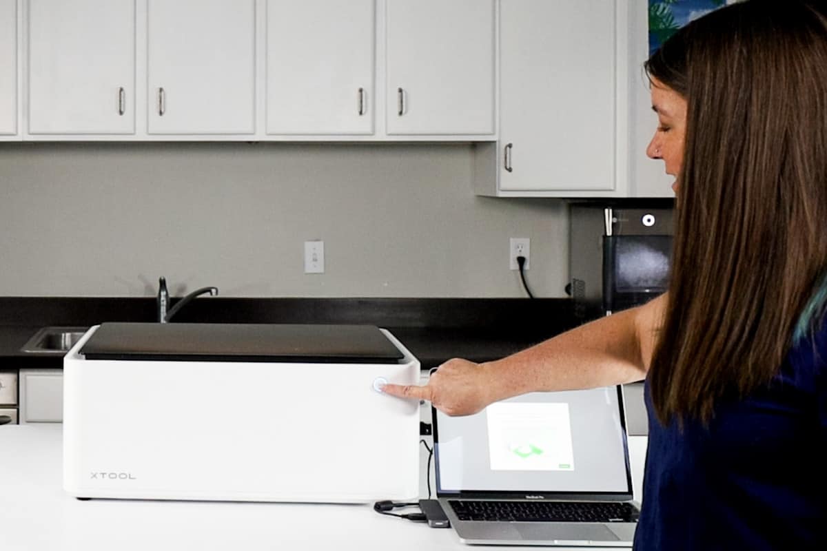 A woman pressing the start button on the front of the xTool M1 laser.