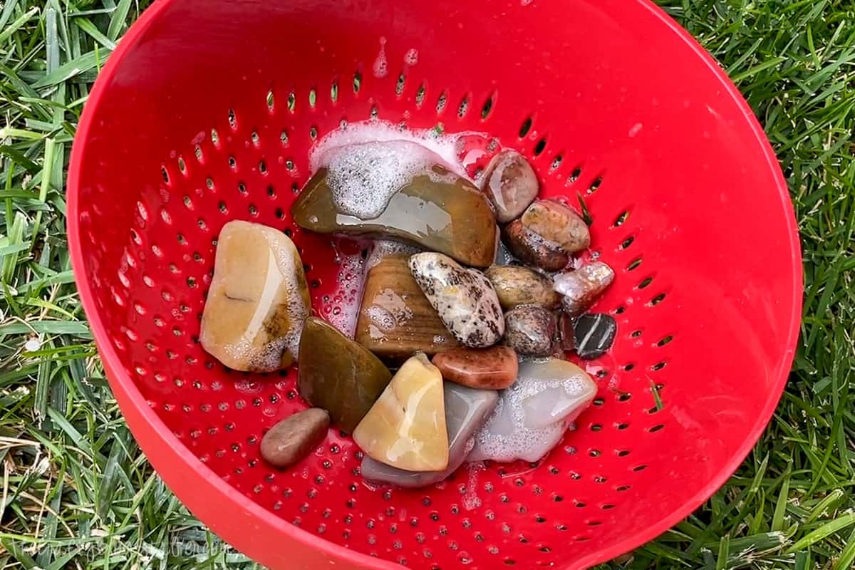 Polished rocks in a red plastic strainer.