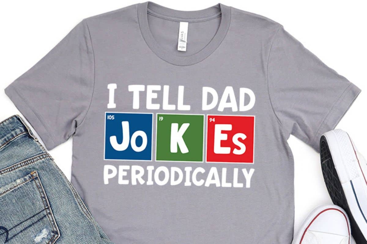 A flay lay with a gray t-shirt with a design that reads" I Tell Dad Jokes Periodically".