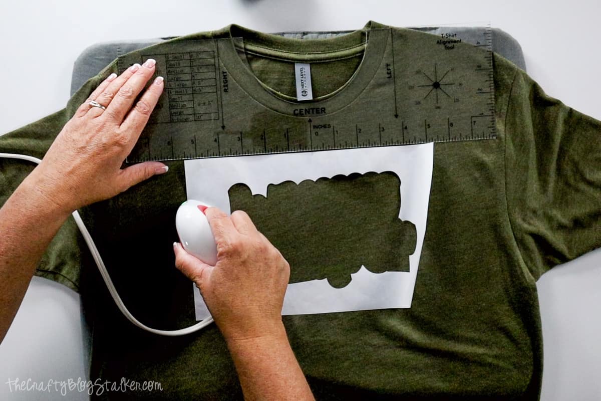 Ironing the the outline of the happy camper stencil onto a t-shirt with the EasyPress mini,