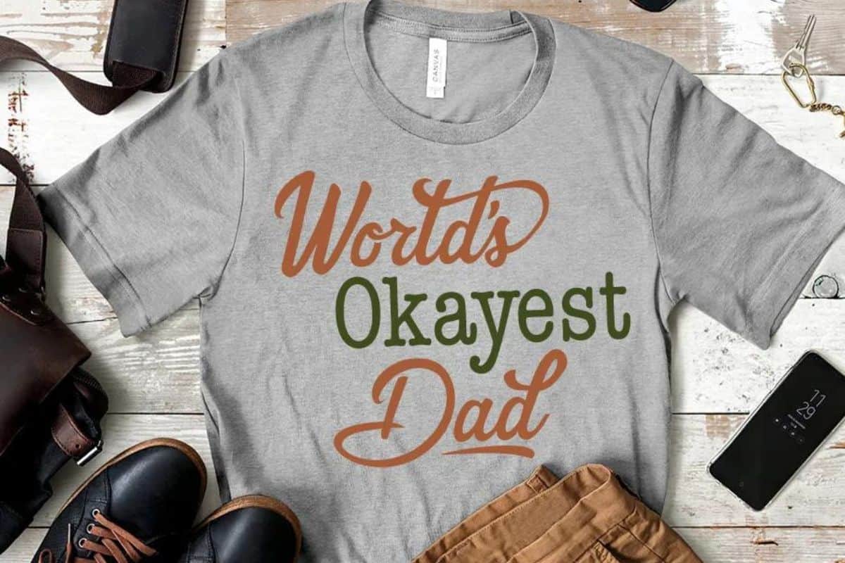 Flay lay with a gray t-shirt and a design that reads "World's Okayest Dad".