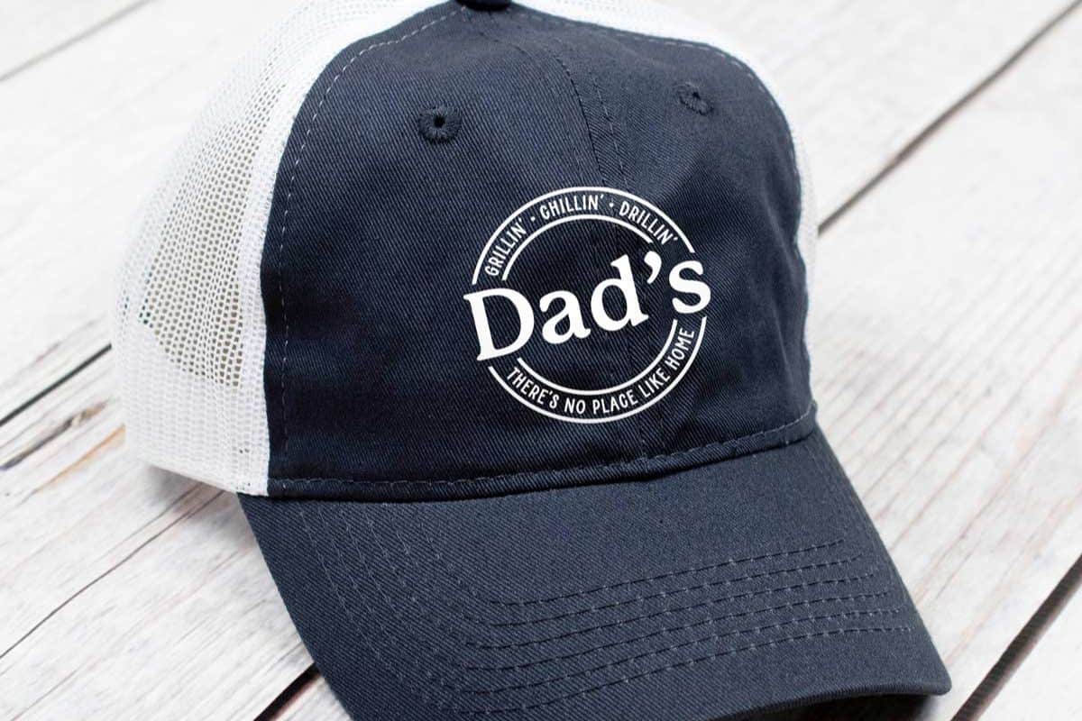 A blue and white cap with a design that reads "Dad's Grillin' Chillin' Drillin' There's no place like home".