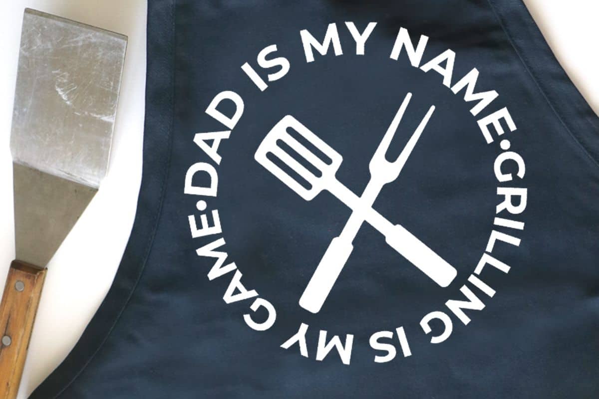 A black apron that reads "dad is my name. Grilling is my game".