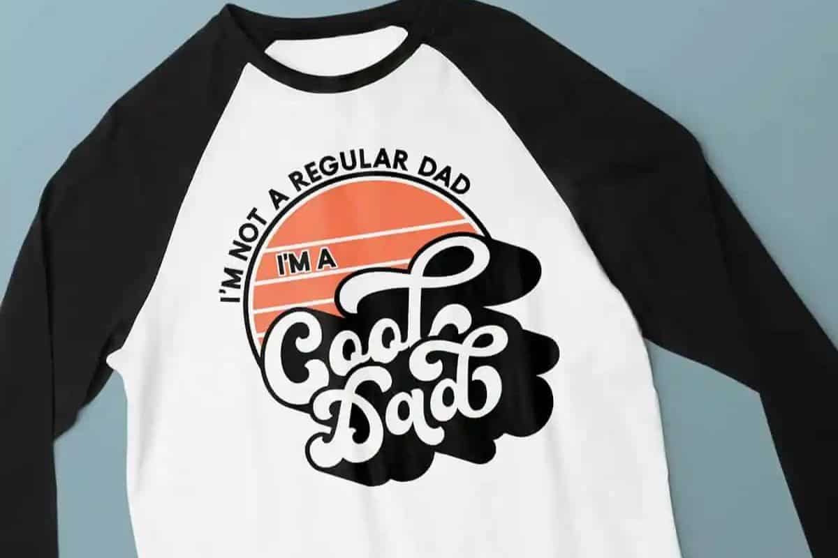 Flay lay with a white and black baseball tee with a design that reads "I'm not a regular dad, I'm a cool dad".