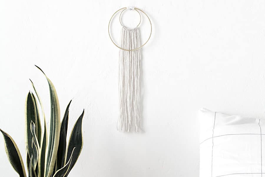 White yarn wall hanging with gold rings.