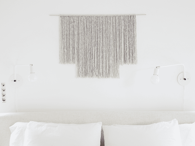 Gray DIY Woven Wall Hanging hanging above a bed.