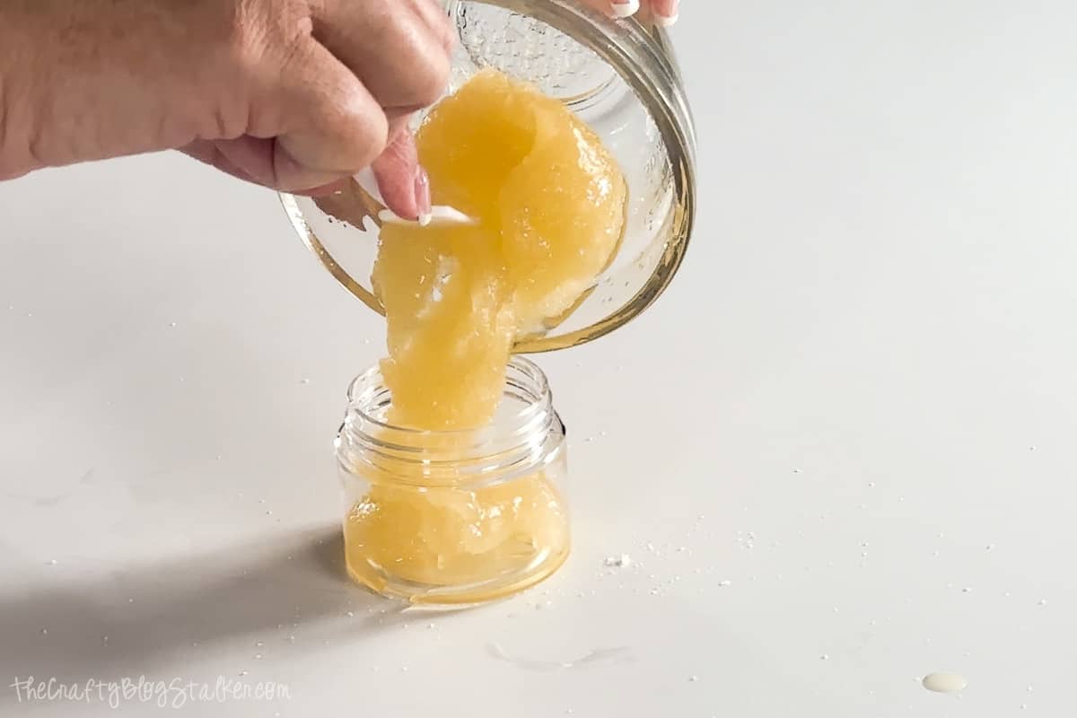 Pouring lip scrub mixture into a 2ounce container with a screw-on lid.