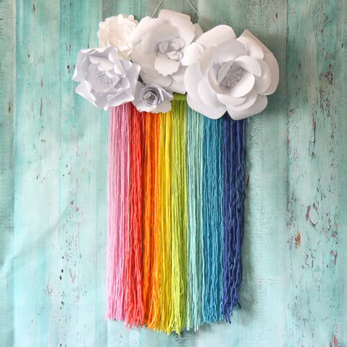 Rainbow macrame wall hanging with white paper flowers.