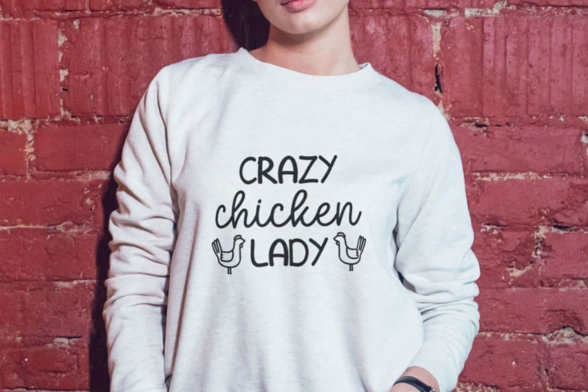 Woman wearing a white sweatshirt with a design Crazy Chicken Lady.