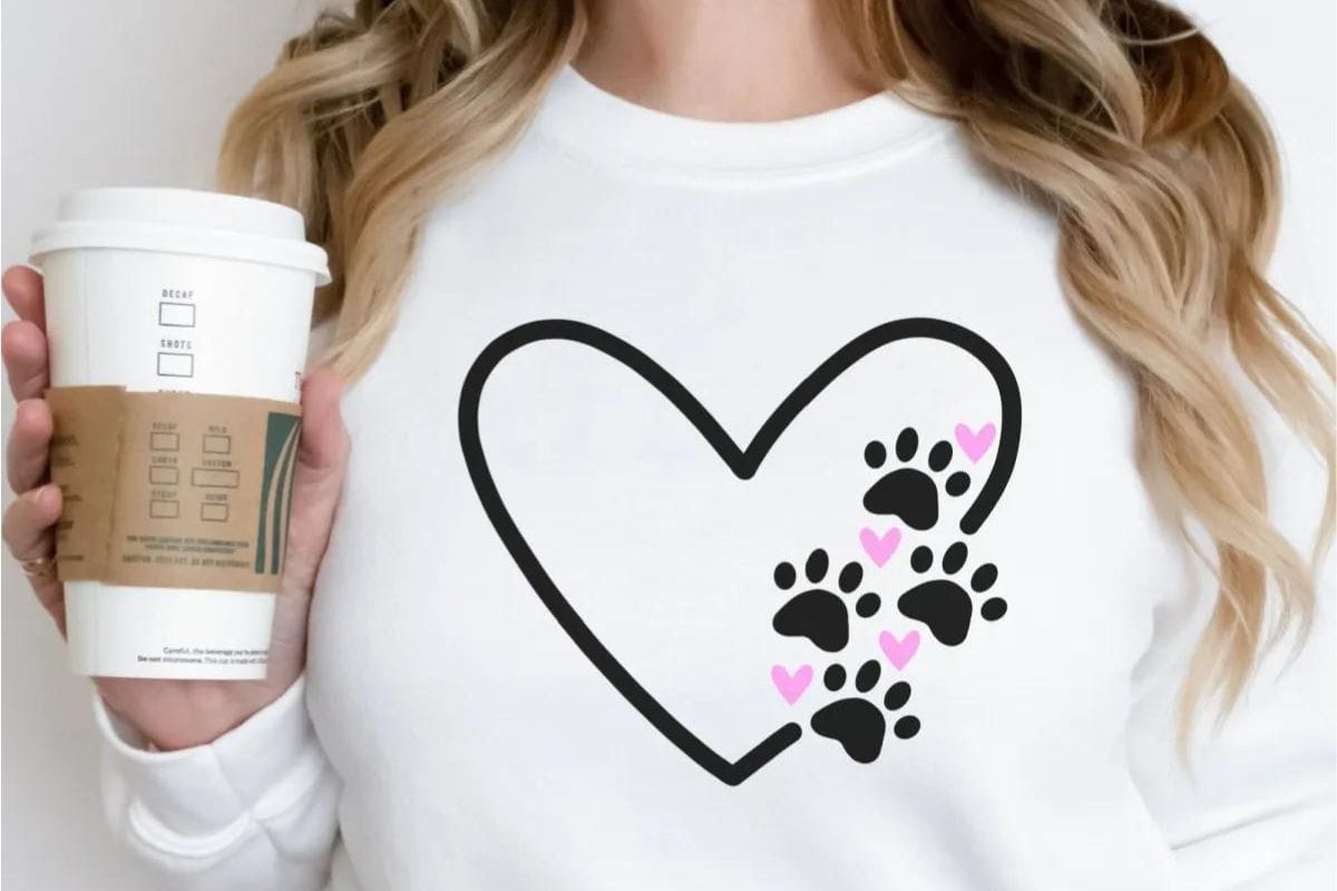 A woman holding a coffee wearing a sweatshirt with a paw print heart design.