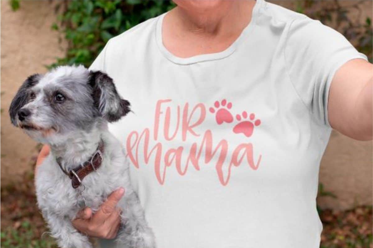 A woman holding a dog and she wearing a shirt that reads 'fur mama'.